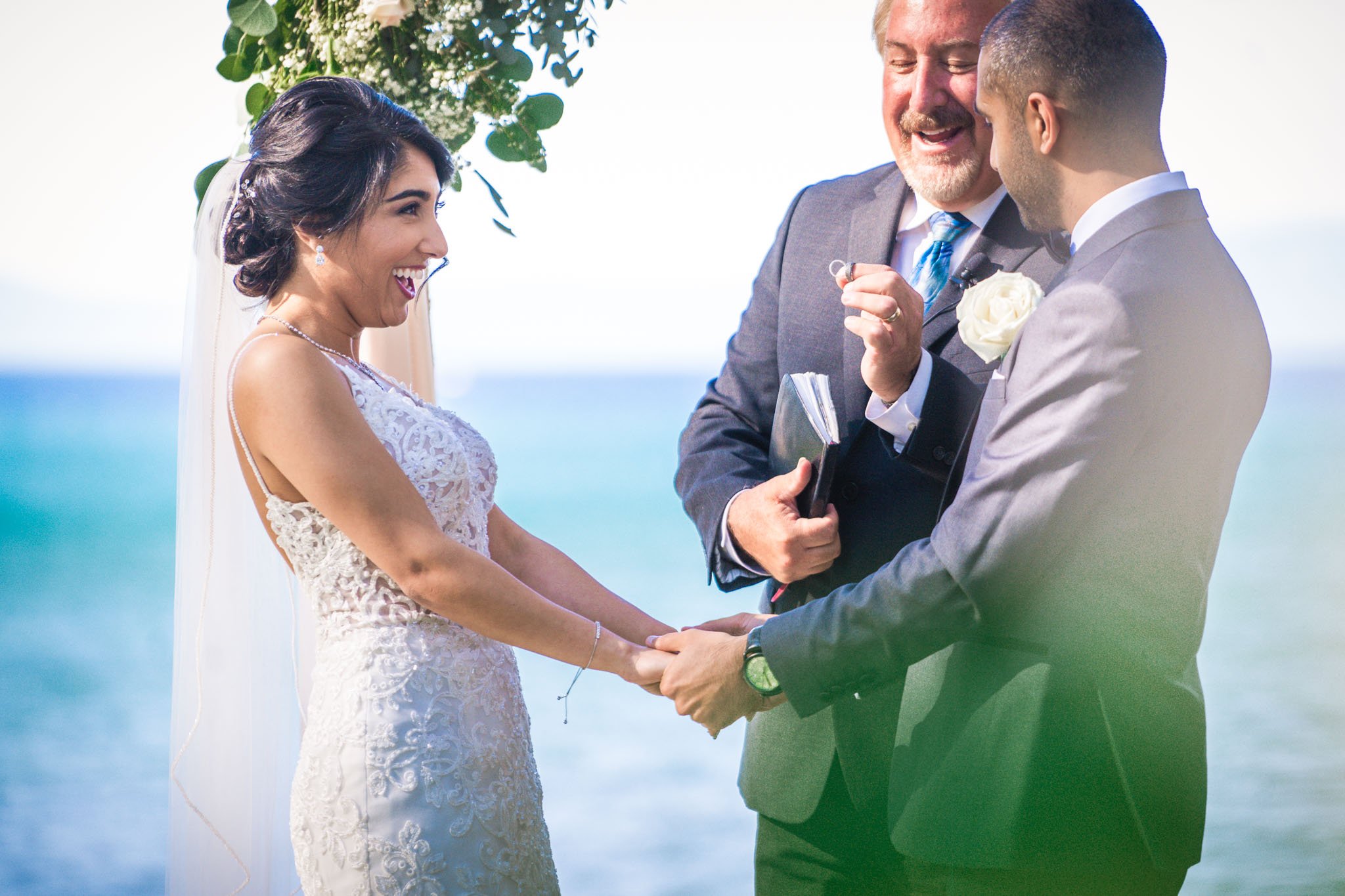 Bride and groom hold hands as the rings are exchanged at their wedding at Regan Beach