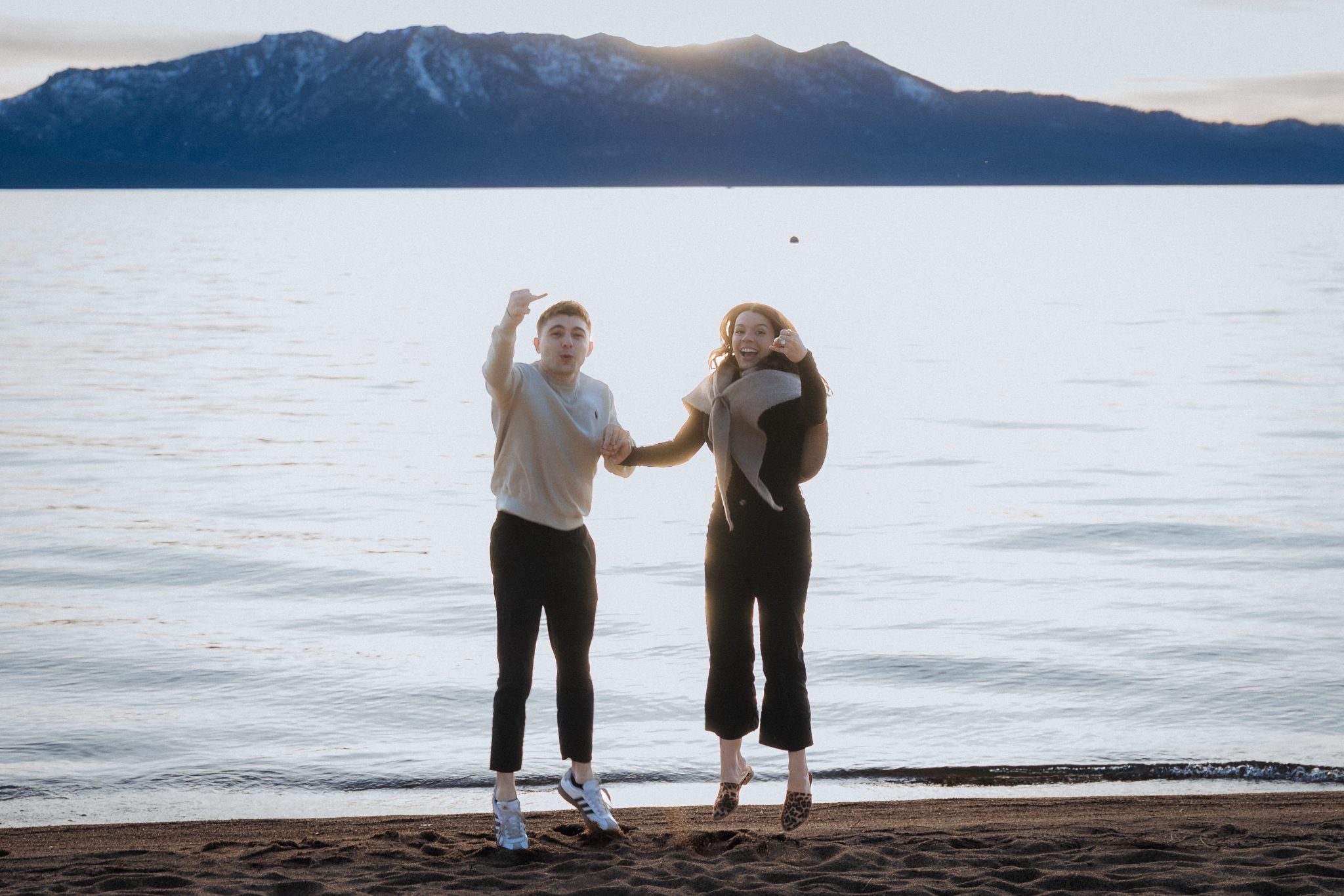 Edgewood Tahoe Lake engagement session featuring a couple celebrating by the Lake Tahoe shoreline with mountain views.