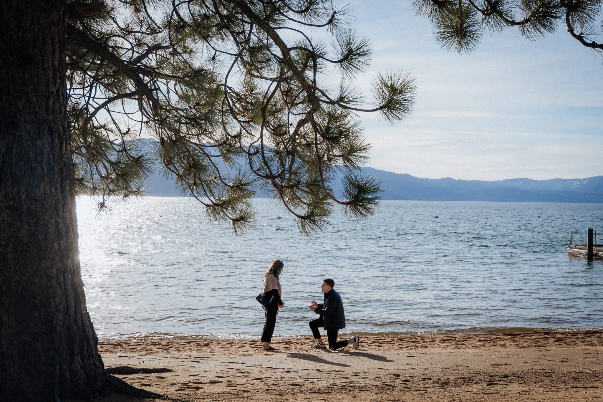 Surprise proposal during an Edgewood Tahoe Resort engagement on the beach with Lake Tahoe and mountain views in the background.