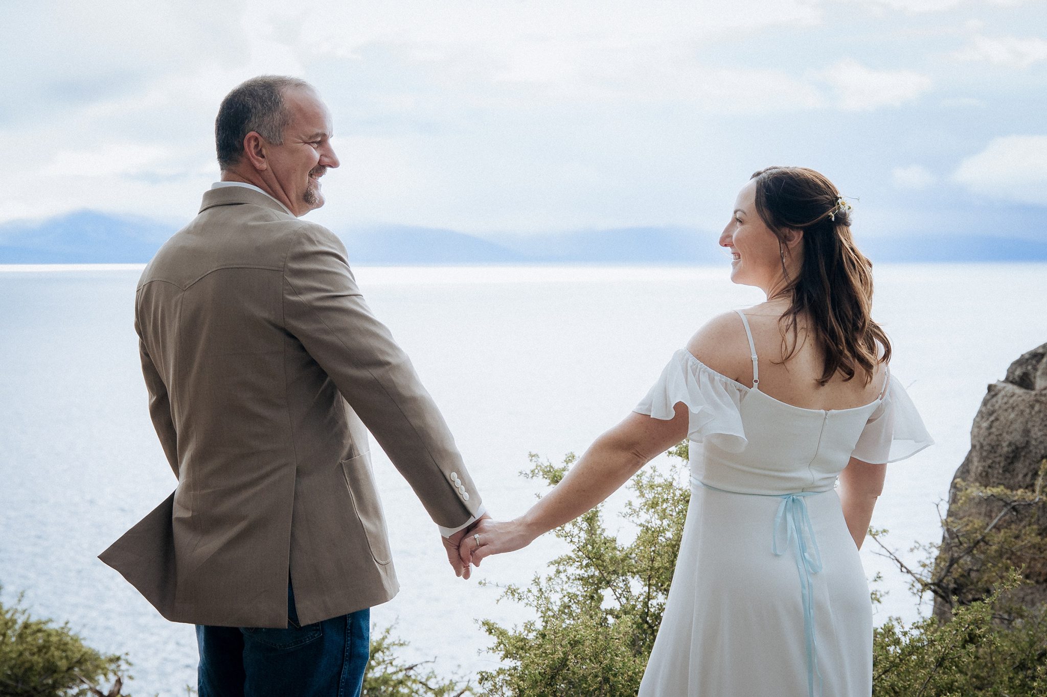 bride and groom holding hands on a scenic Lake Tahoe overlook, demonstrating how to look natural in wedding photos through genuine connection and relaxed interaction