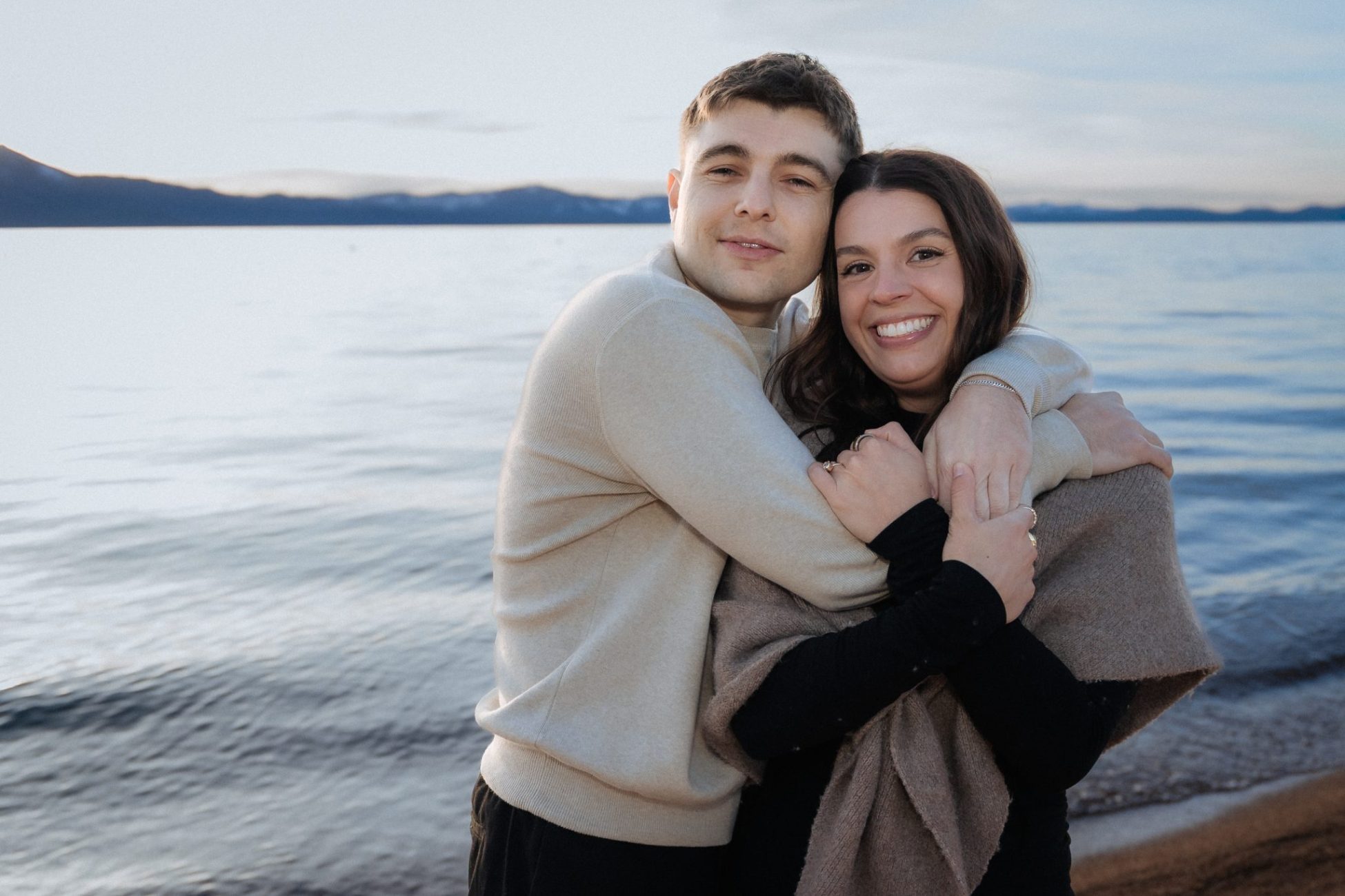 Lake Tahoe engagement portraits of a smiling couple embracing by the shoreline during an Edgewood Tahoe Resort engagement session.
