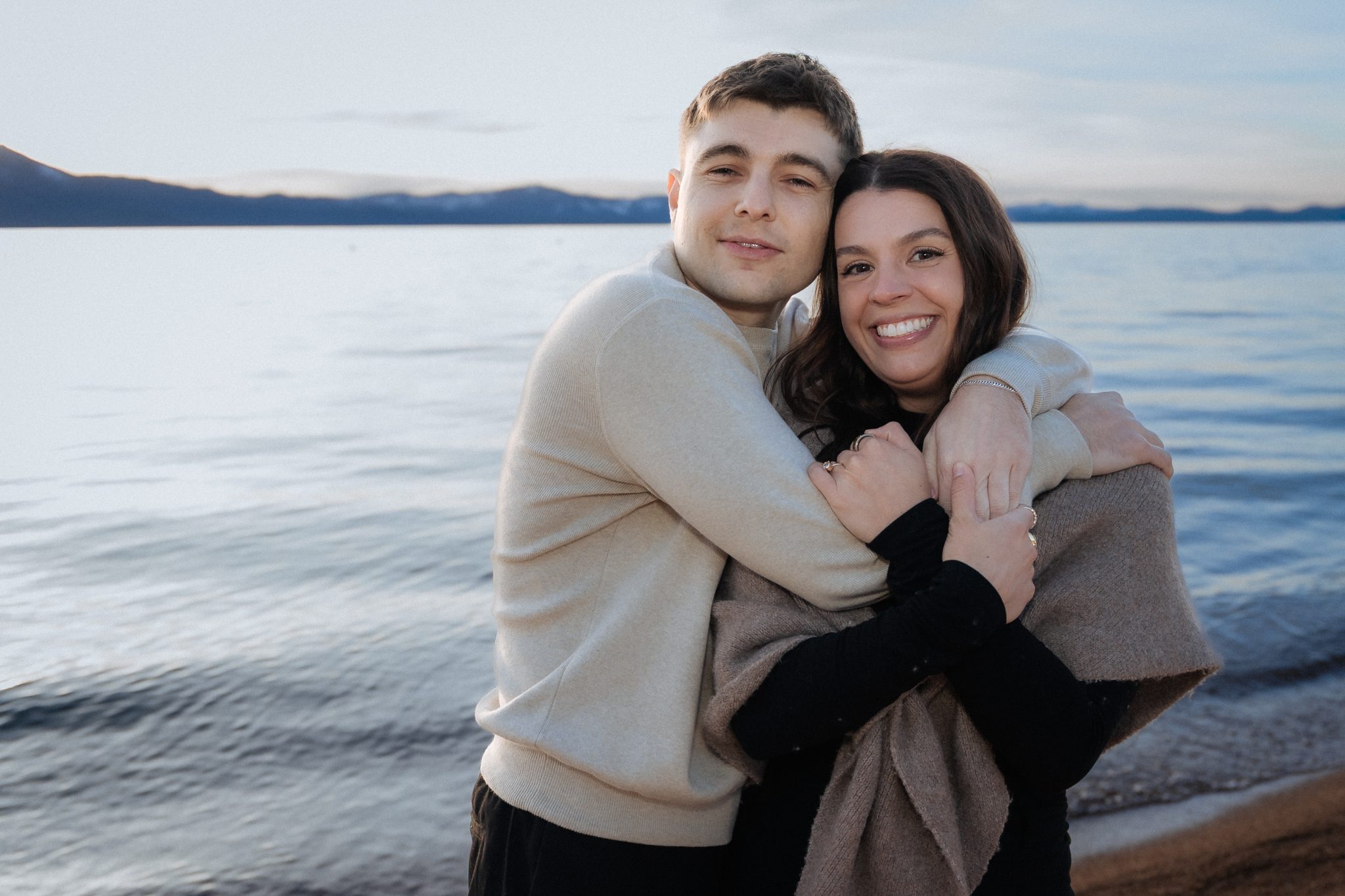 Lake Tahoe engagement portraits of a smiling couple embracing by the shoreline during an Edgewood Tahoe Resort engagement session.