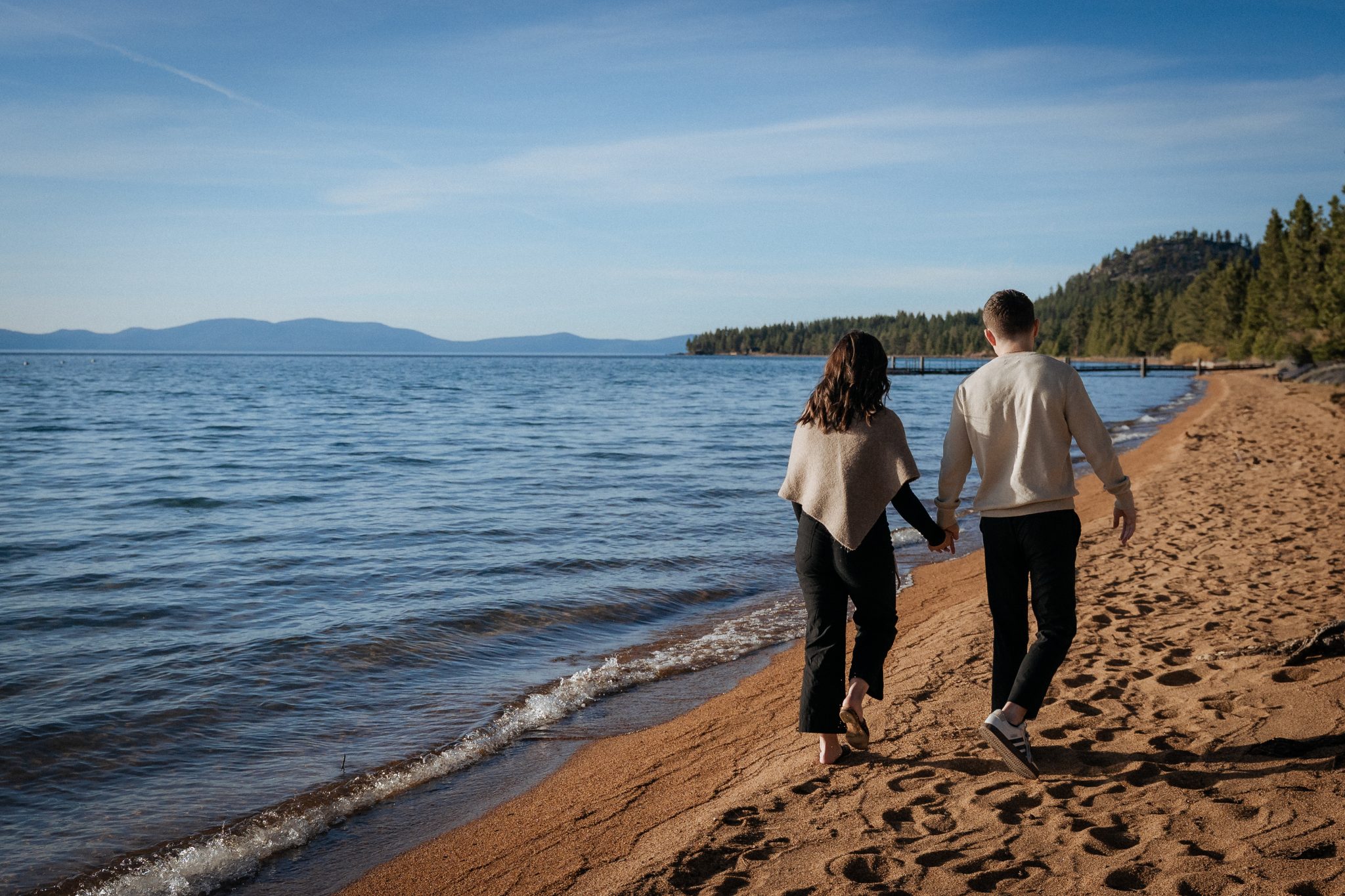 Couple walking along a Lake Tahoe proposal location at Edgewood Tahoe Resort before their romantic engagement.