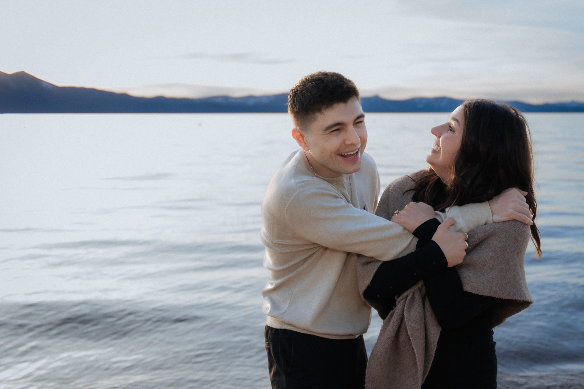 Romantic Edgewood Tahoe proposal featuring a joyful couple embracing by the Lake Tahoe shoreline at sunset.