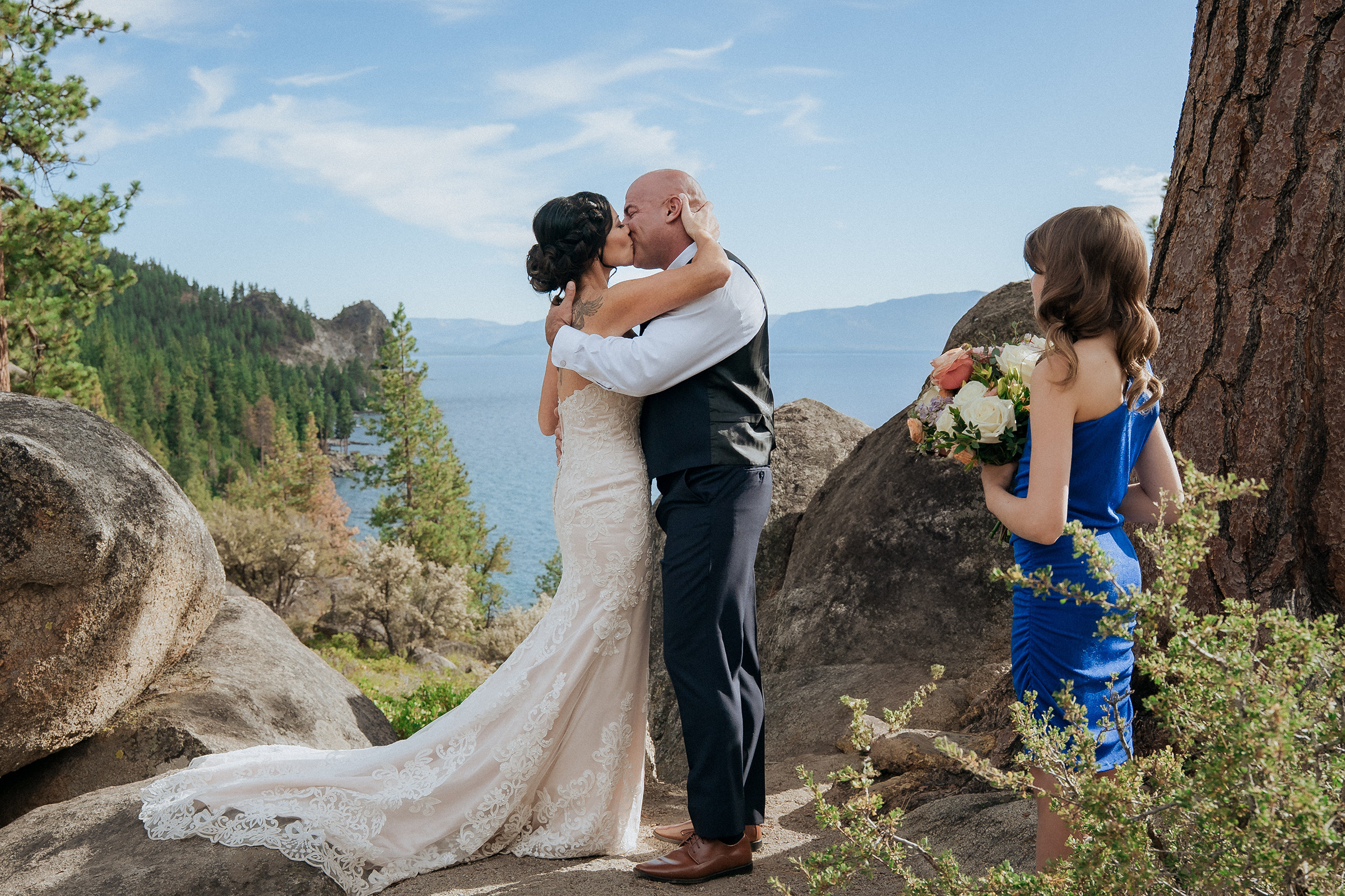 Logan Shoals wedding ceremony moment with the newlywed couple embracing while a guest photographs them among scenic rocks overlooking Lake Tahoe.