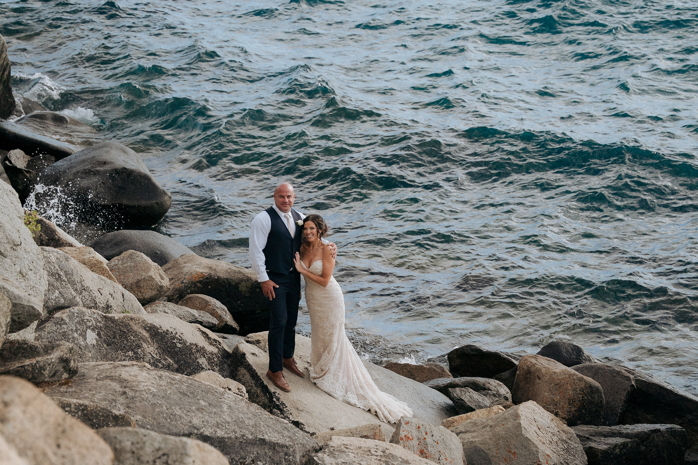 Logan Shoals wedding couple standing together on the rocky Lake Tahoe shoreline with scenic water and mountain views.