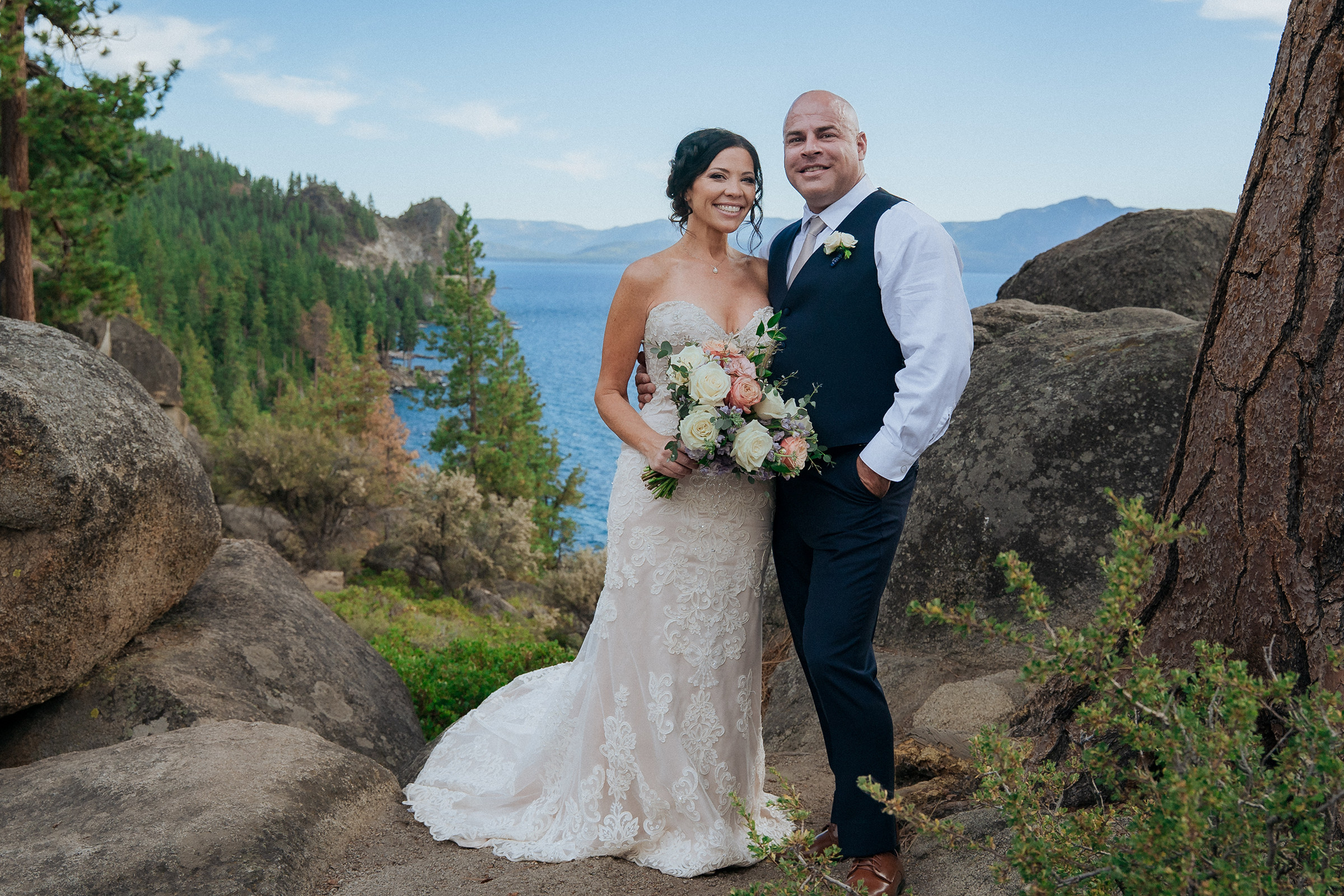 Logan Shoals wedding photography featuring a newlywed couple posing with a bouquet among scenic rocks overlooking Lake Tahoe and mountain views.